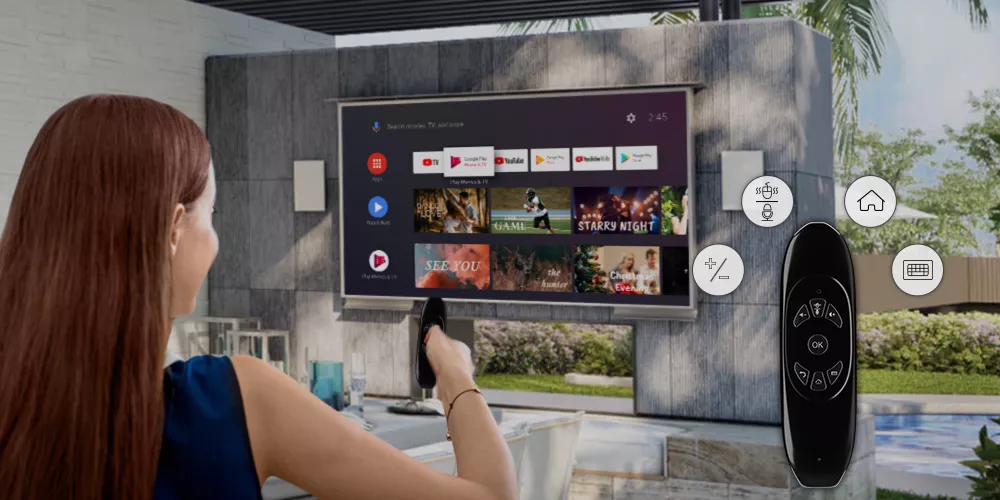 Woman watching in a backyard on her outdoor TV while holding a remote control.