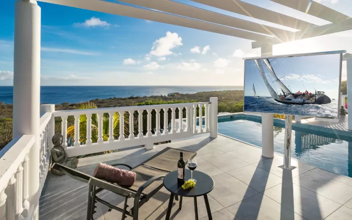 Patio with ocean view, pool, lounge chair, and floor-mounted outdoor TV displaying a sailboat race.