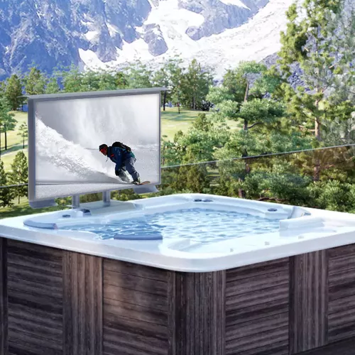 A wooden deck with a hot tub sitting on top and an outdoor TV next to a mountain range.