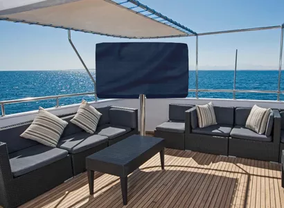 Preview of a yacht deck with elegant couches, tables, and outdoor TV with its sunbrella cover.