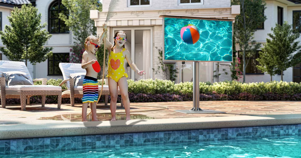 Two kids having fun in the pool with a self-standing outdoor TV nearby.