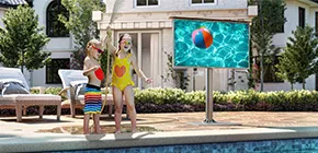 Two children joyfully enjoying the pool with a self-standing safety outdoor TV nearby.