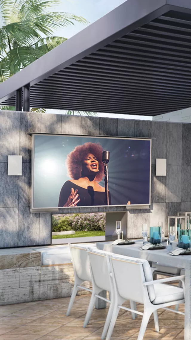 Fancy outdoor dining next to a Cosmos TV shows a singer on its screen.