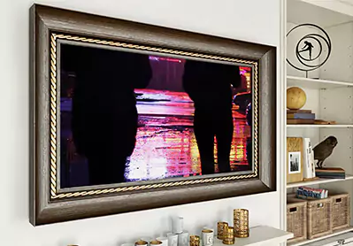 TV espejo con marco negro sobre una pared blanca con una librera a un lado.