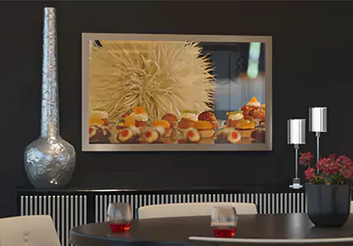 TV espejo inteligente con marco sobre una pared negra con un jarrón de metal multi-tono con flores.