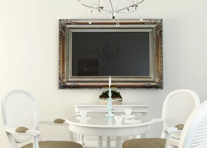 Un TV espejo con marco montado en la pared con sillas de ratán blancas y una mesa circular.
