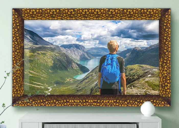 Un TV espejo enmarcado colocado en una pared sobre un gabinete blanco muestra a un hombre de pie frente a una montaña.