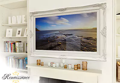 TV espejo inteligente con marco blanco sobre una pared lisa con estantes a los lados y velas doradas.