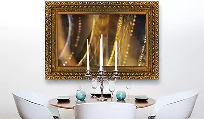 Un gran TV espejo con marco de madera dorada montado en una pared blanca sobre una mesa redonda.