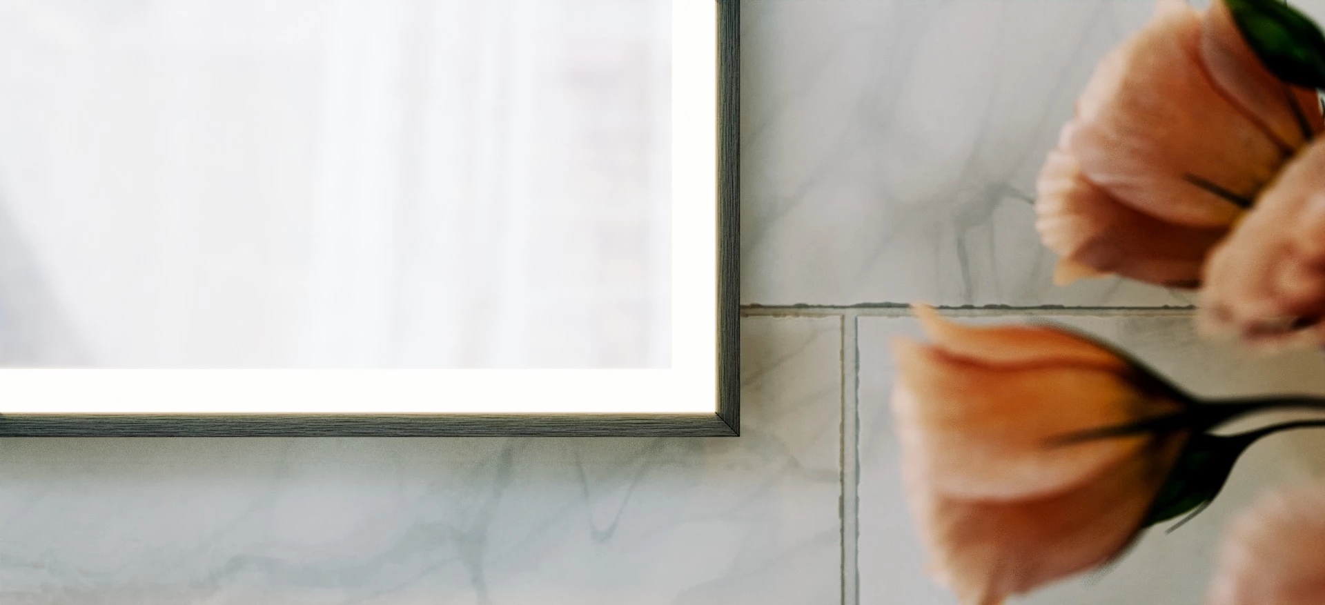 Wooden framed lighted mirror attached to a marble wall with flowers beside in Abu Dhabi.