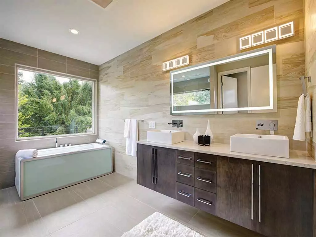 Bathroom with a large square shaped window above a bathtub and an energy efficient mirror in Ajman.