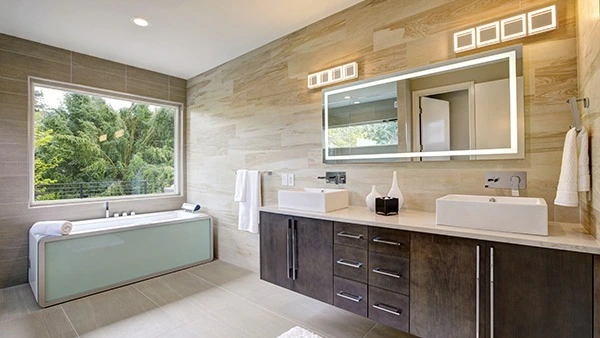 Icon of bathroom with a large window above a boxy bathtub and a custom lighted mirror in Ajman.
