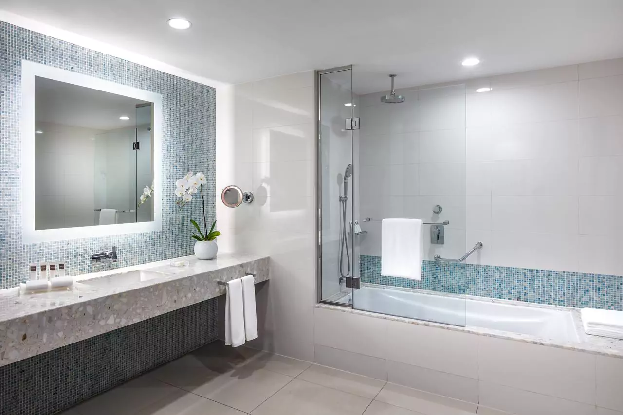 A stylish bathroom with a bathtub and a sink with a frameless backlit mirror for hotels in Al Ain.