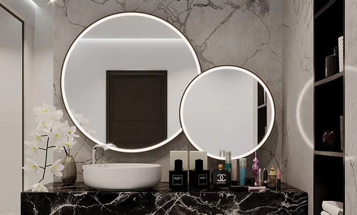 Tiny of two unequal size round lit mirrors with a sink and perfumes on a marble countertop in Al Ain.