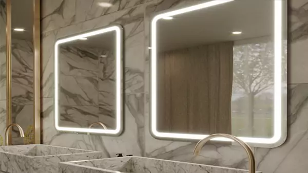 Two lighted mirrors with round edges inset on a marble tiled wall and two marble sinks in Bahrain.
