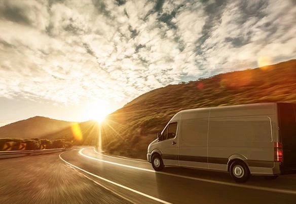 A white van driving along a curved highway at sunset beside a hill under a  cloudy sky in Qatar.