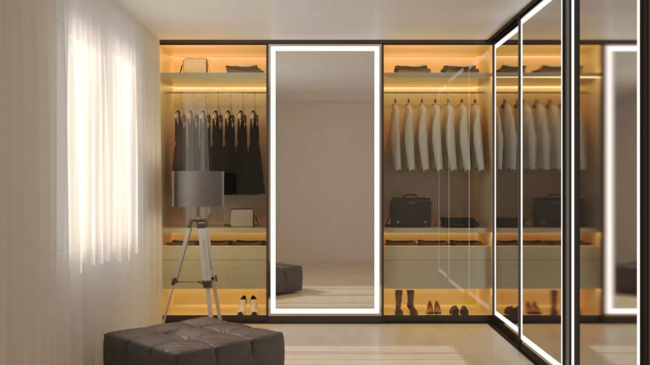 Dressing room in Oman with a closet full of hung clothes, lighted mirrors, and a leather stool.
