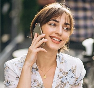 Woman with short brown hair talking on a smartphone while smiling, wearing a floral dress in Dubai.