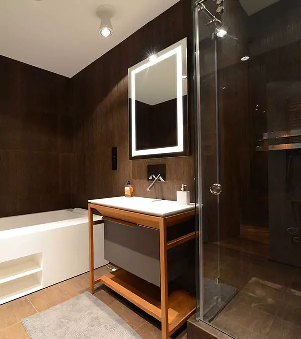 Icon of bathroom in a hotel room with a boxy bathtub beside a lighted mirror above a sink in Dubai.