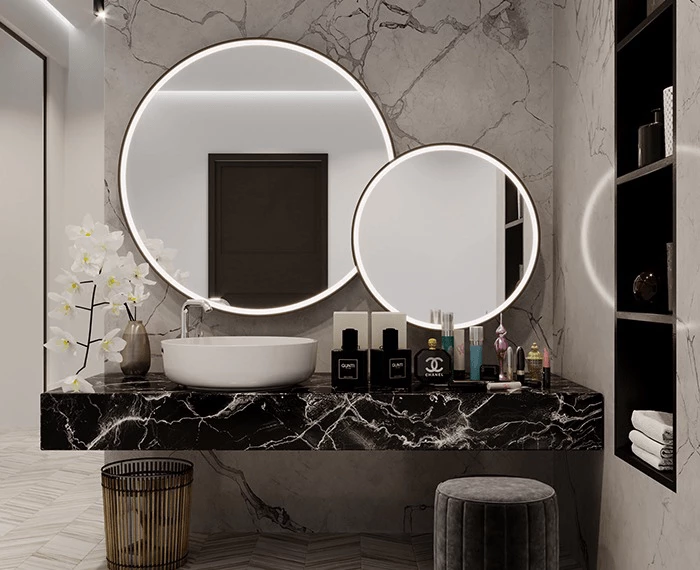 Two different sized oval lighted mirrors mounted on a white marble wall with a single sink in Dubai.