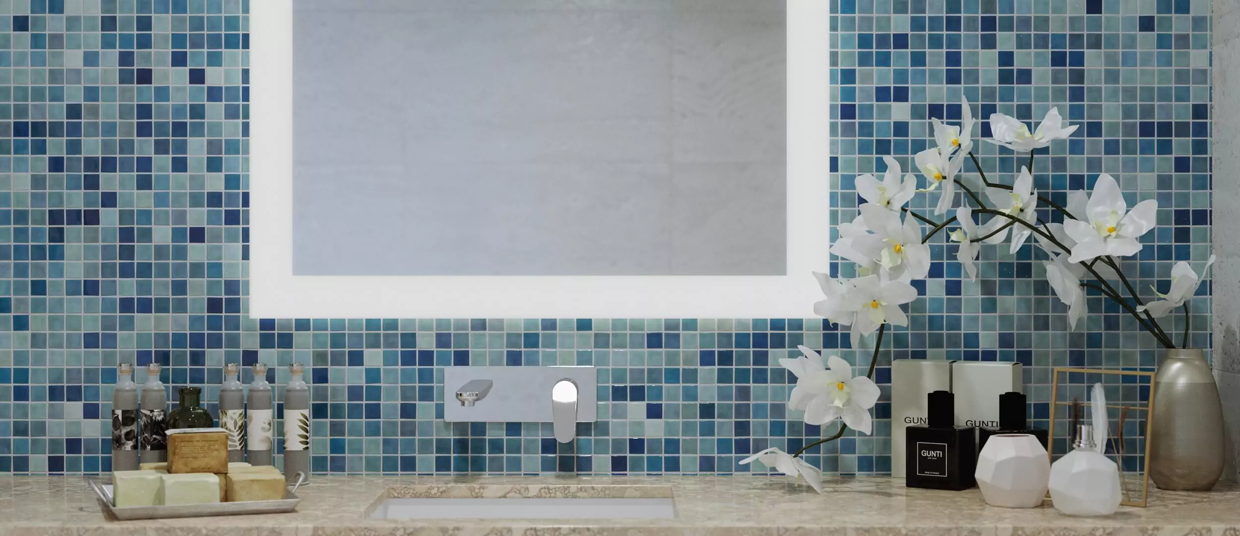 Custom frosted mirror mounted on a blue mosaic tiled wall and bathroom essentials below in Dubai.