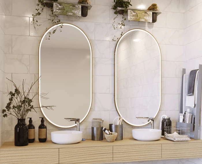 Oval lighted mirrors mounted on a tiled wall with bathroom items beside the two sinks in Qatar.