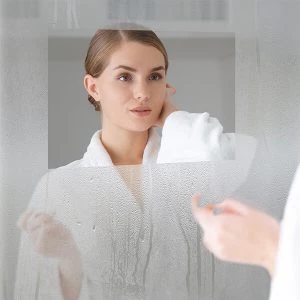 Vanity mirror with a defogger and a woman in a white bathrobe looking at the mirror in Oman.