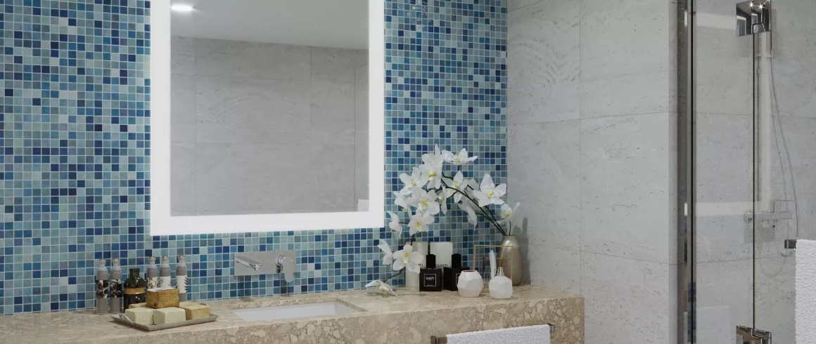 Lighted mirror set on a blue mosaic tiled wall beside glass shower room in a bathroom in Kuwait.