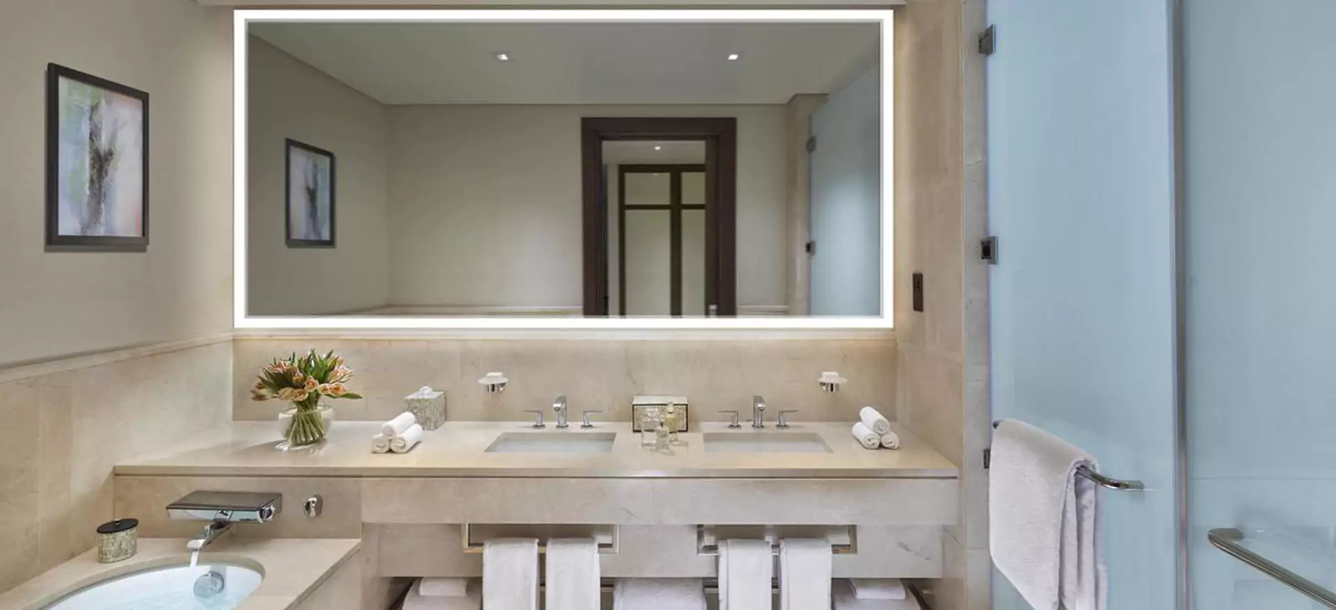 Ceramic tiled bathroom with a bathtub and large Grand Mirrors Lux above a pair of sinks in Dubai.