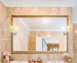 A thumb of golden-framed mirror with a decorative salano lamp set on the wall above a basin.