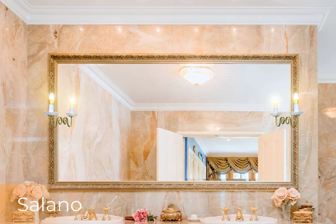Ajman chic vanity mirror with led lights in a golden frame and wall mounted salano lamp above sink.