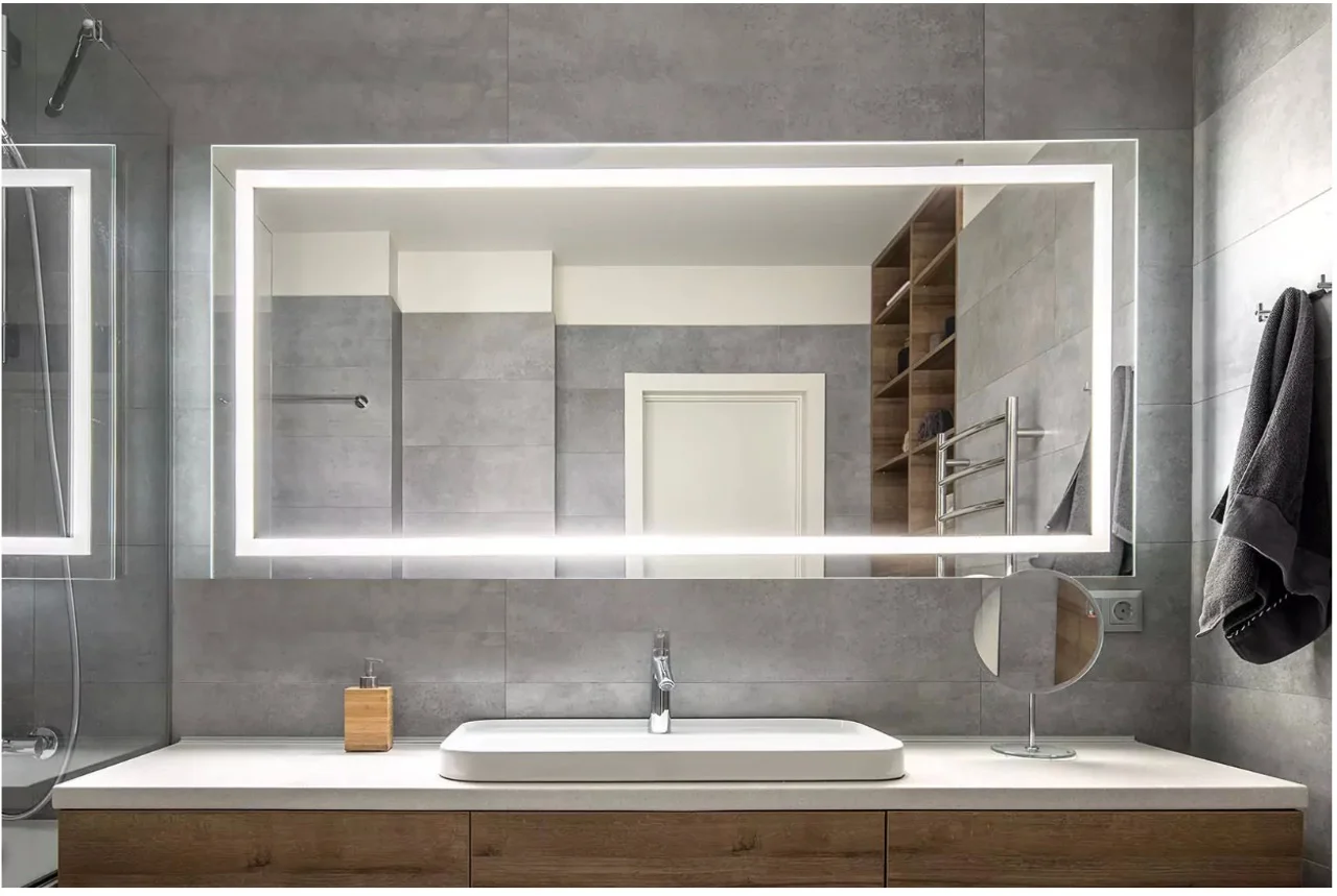 Lighted mirror set on a blue mosaic tiled wall beside glass shower room in a bathroom in Kuwait.