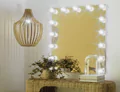 Tiny of Hollywood mirror facing a wooden elipsa pendant light with a rattan table and stool in Oman.
