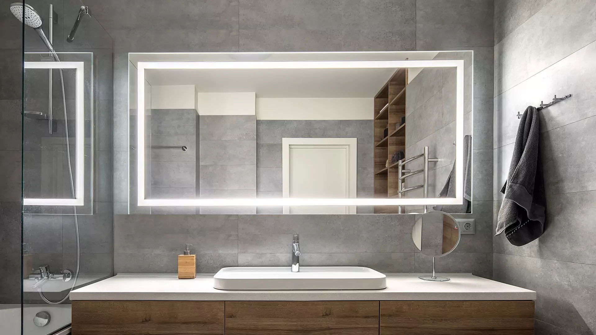 Grand mirrors lux in Oman mounted on a concrete wall above a sink and a shower room at the side.
