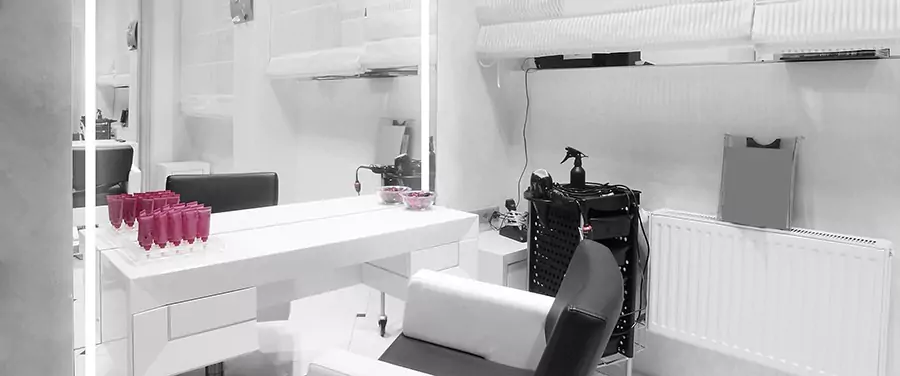 Salon with a lighted mirror above a laminate cabinet with hair products and a salon chair in Oman.