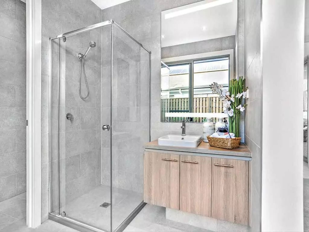 Bathroom with a glass shower room beside a custom lighted mirror above a wooden cabinet in Oman.