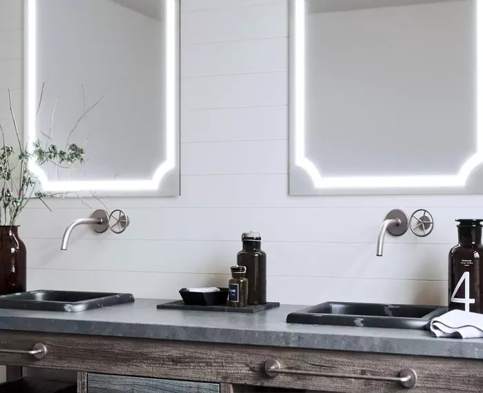 Oman Grand Mirrors Lux inset on a white ceramic tiled wall above a concrete countertop with sinks.