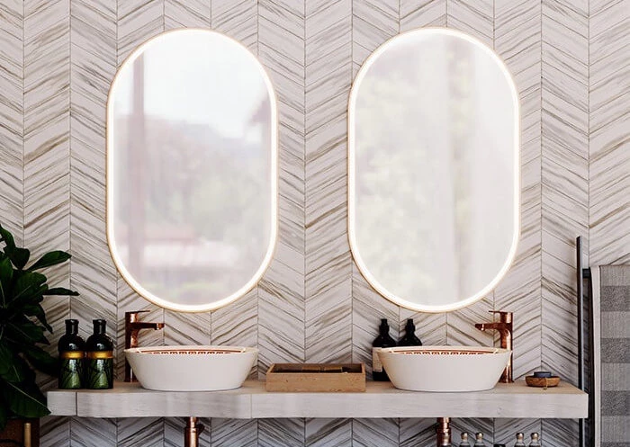 Tiny of two oval lit mirrors mounted to a stylish wall and a dual sink vanity in Ajman.
