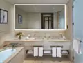 Tiny of bathroom with a bespoke lighted mirror, a bathtub, and two sinks with towels below in Qatar.