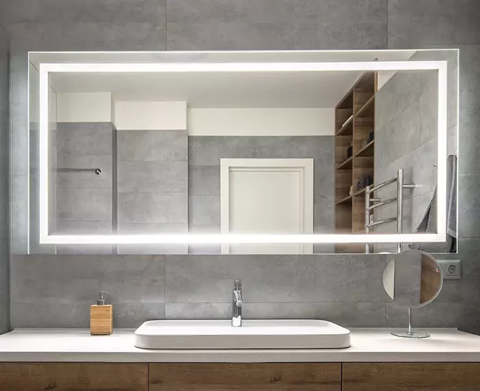 Rectangular custom lighted mirror on a concrete wall above a solid surface material sink in Qatar.