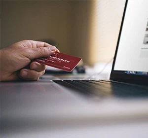 A man's hand holding a red credit card next to an open laptop on a desk in Qatar.