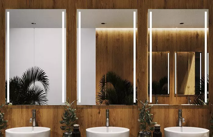 Three boxy frameless backlit mirrors mounted on a wooden wall with white washbowls below in Dubai.