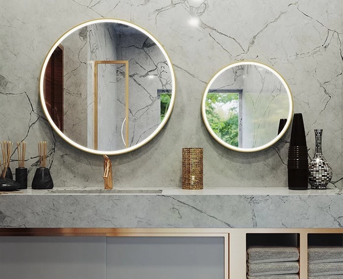 Oval lit mirrors bound on a marble wall above a gray stone countertop with incense sticks in Dubai.