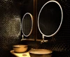 Tiny of black mosaic tiled wall with a pair of gold oval lit mirrors and two gold basins in Al Ain.