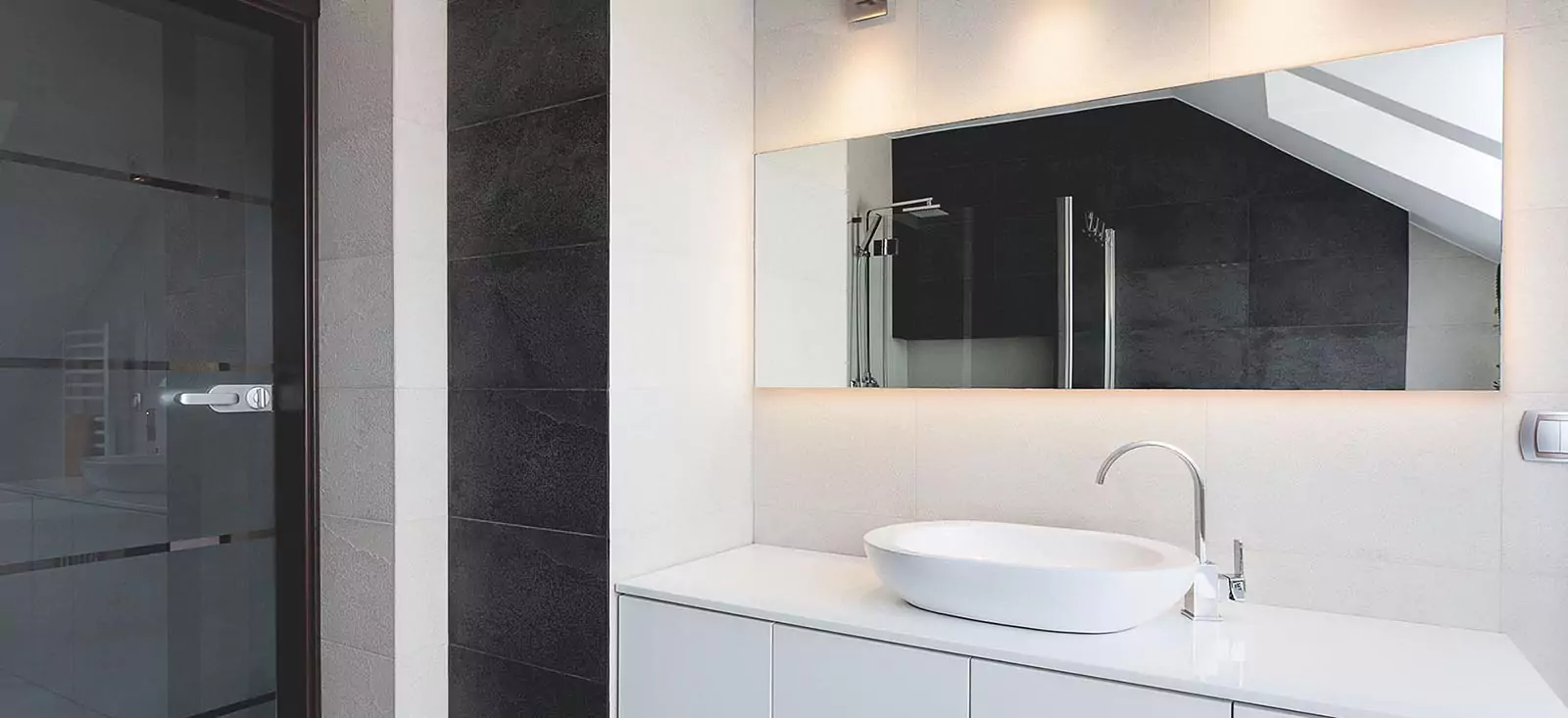 Saudi Arabia stylish bathroom has a single sink and an illuminated mirror mounted on a white wall.