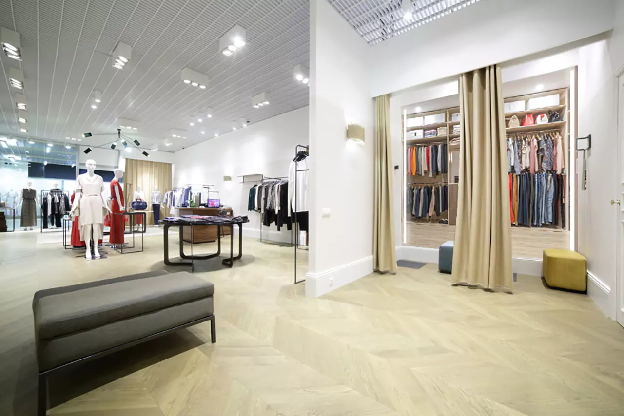 Fitting rooms with lighted mirrors and small sofa stools in a modern clothing store in Saudi Arabia.