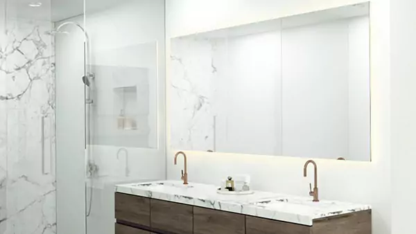 Compact of a frameless backlit mirror above the bathroom sink is installed on a white wall from Sharjah.