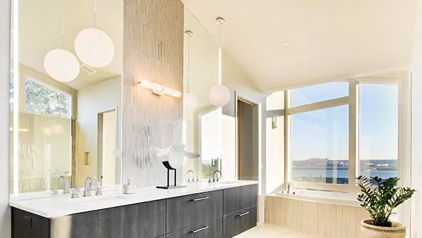 Tiny of bathroom in Sharjah with lighted mirrors above a wooden cabinet with a marble countertop.