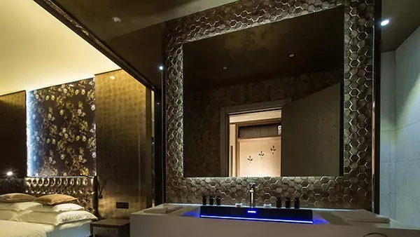 Mini of above a single sink, on a wall with dark hexagon tiles, are lighted mirrors.
