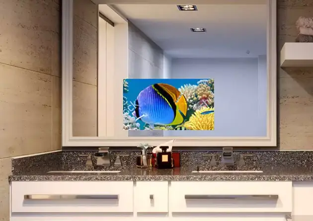 Sobre un lavabo doble con armario se ha instalado un televisor espejo que muestra peces de colores y arrecifes de coral.